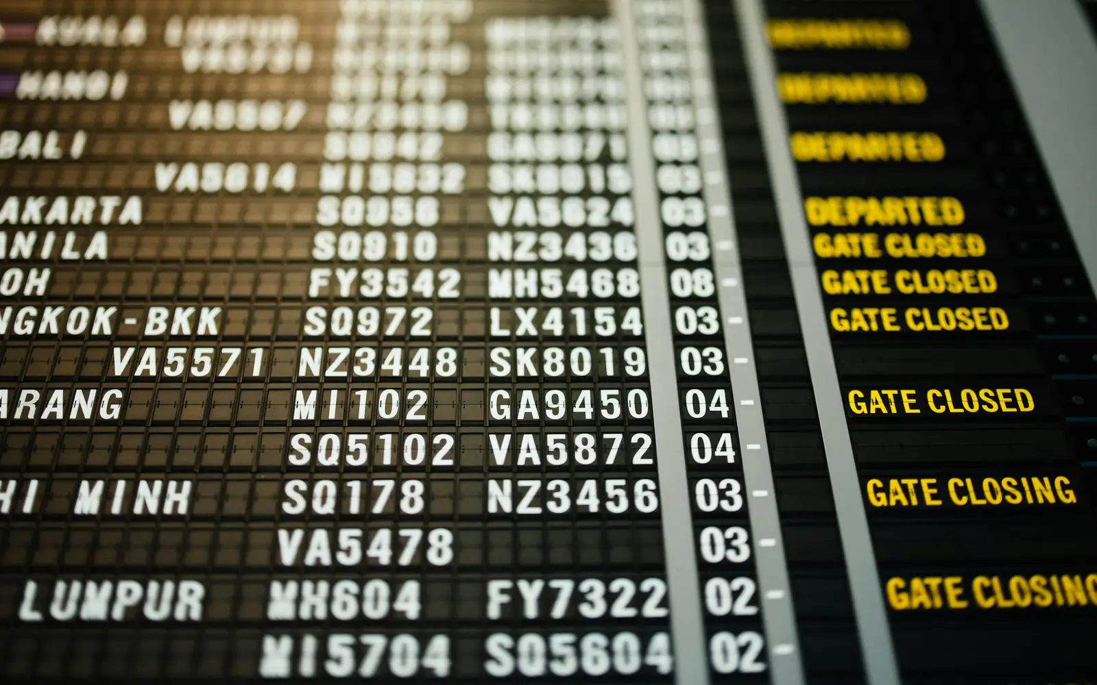 An airport departures board listing flights to Asian cities including Bangkok, Manila and Kuala Lumpur.