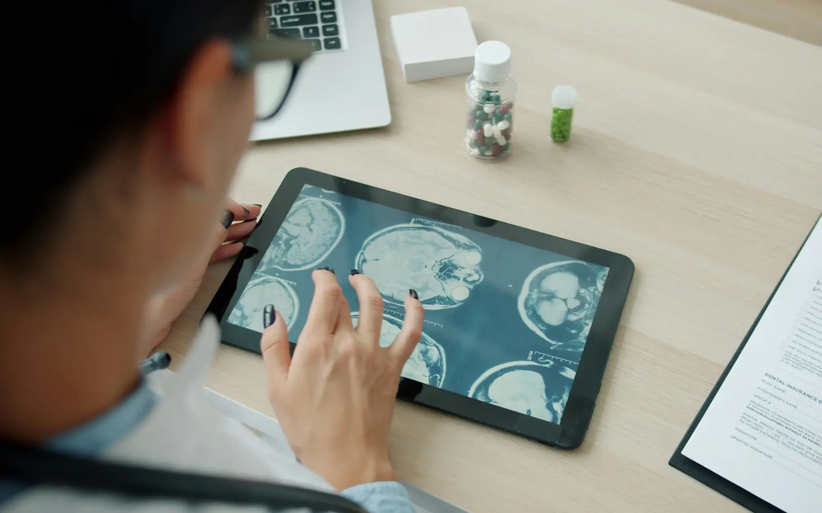 A doctor looks at MRI scans on a tablet next to a clipboard with a form.