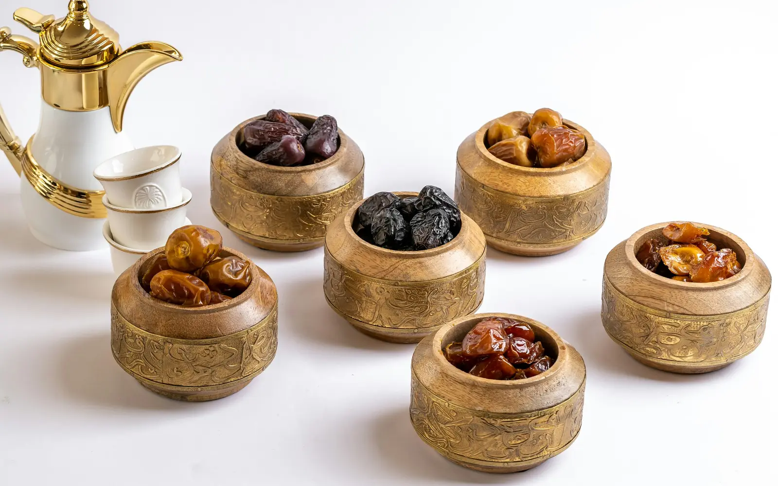 An Arabic coffee pot and small cups beside brass bowls filled with dates.