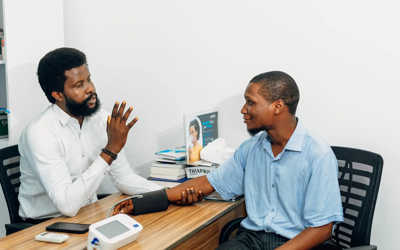 A doctor talks with a patient across a desk while measuring his blood pressure.