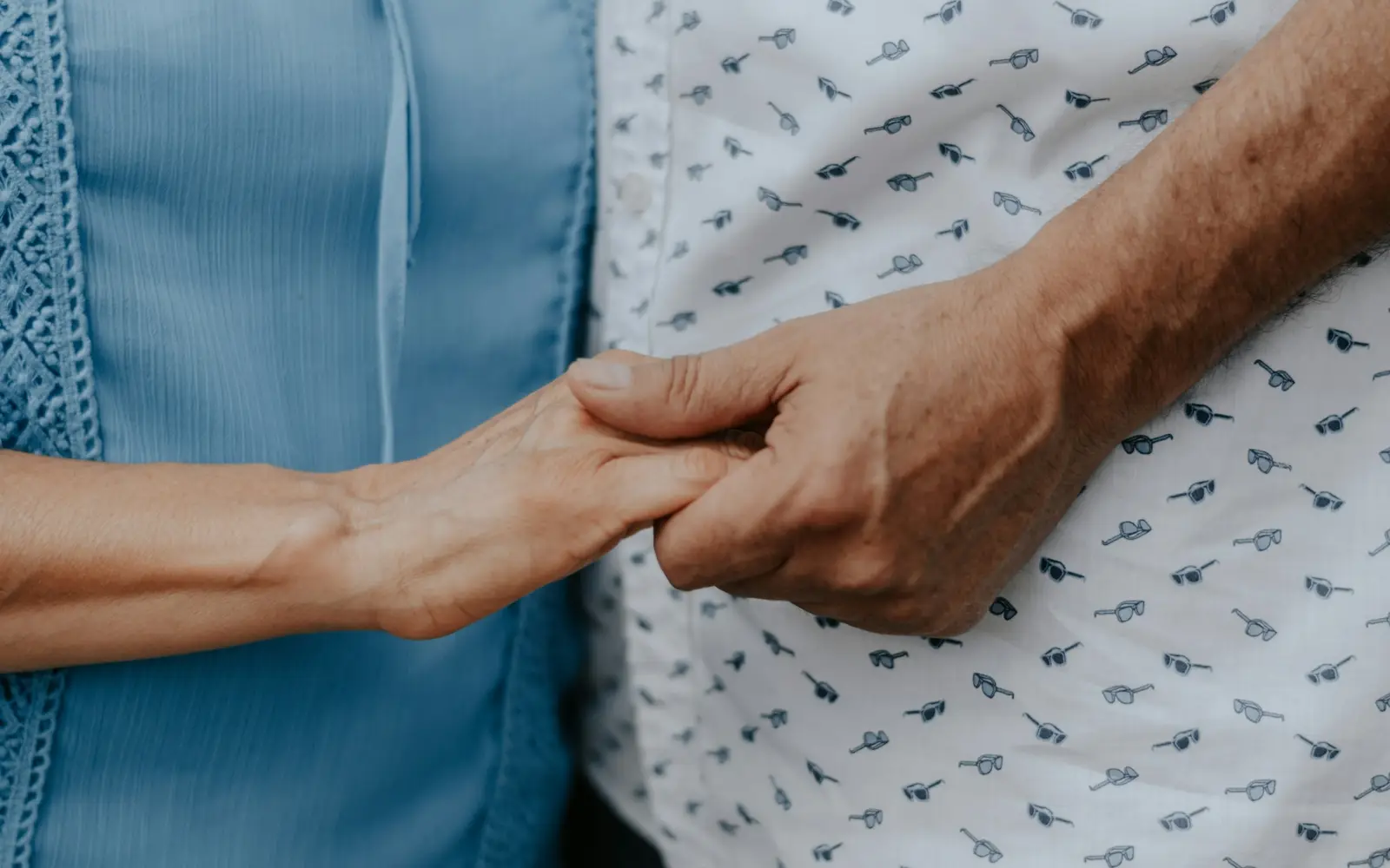 Close-up of two people holding hands, one in a blue shirt and one in a patterned shirt.