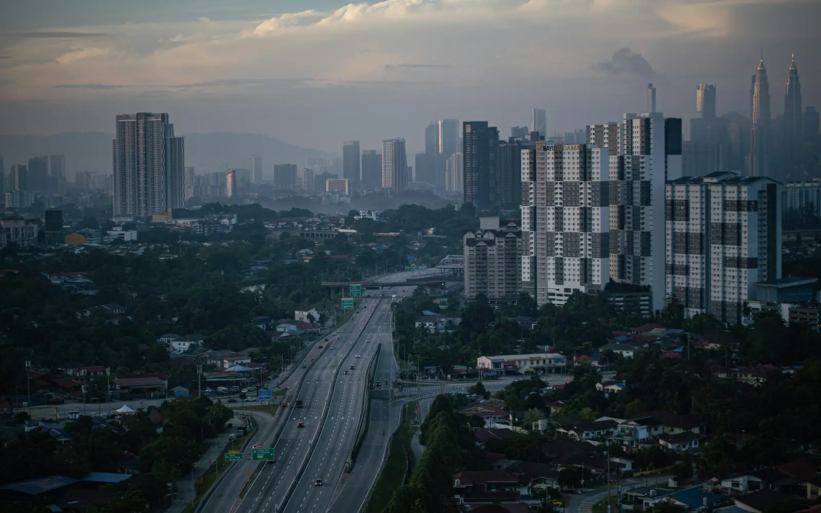 A misty view over Kuala Lumpur with an expressway, apartment blocks and the Petronas Towers in the distance.
