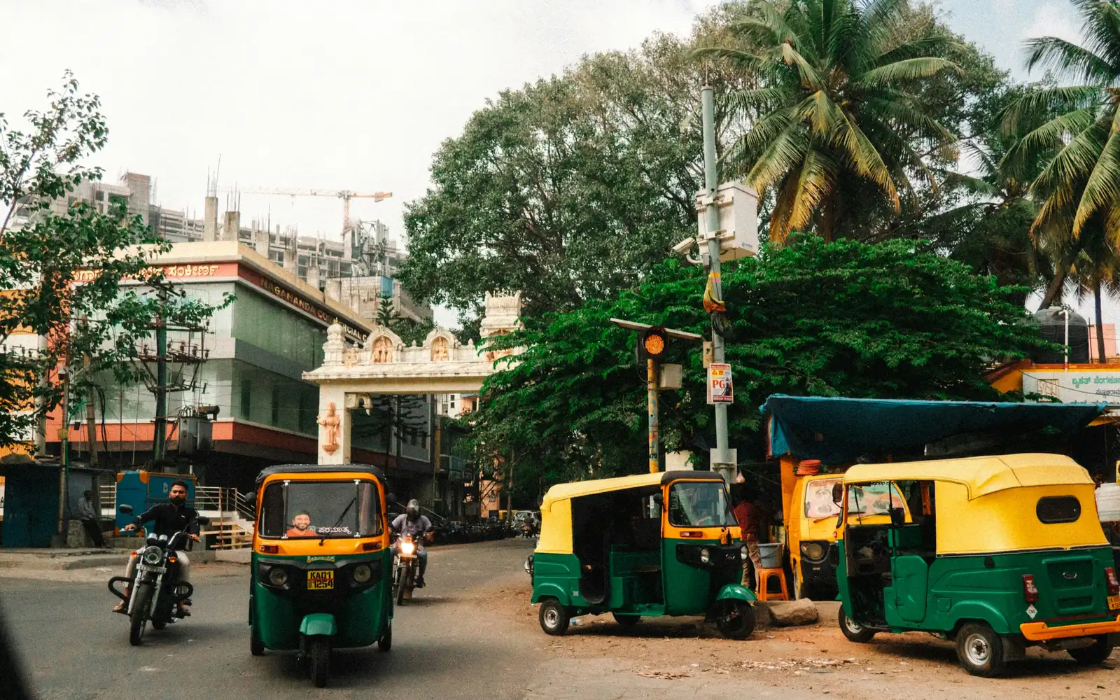 Green and yellow auto-rickshaws and motorbikes on a tree-lined street in an Indian city.