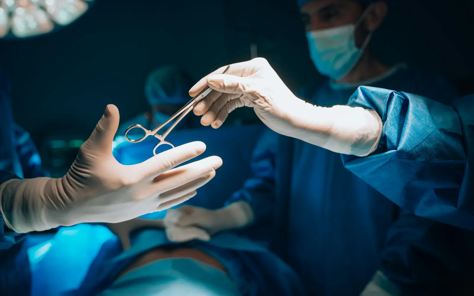 Gloved hands pass a surgical instrument between members of a surgical team in an operating room.