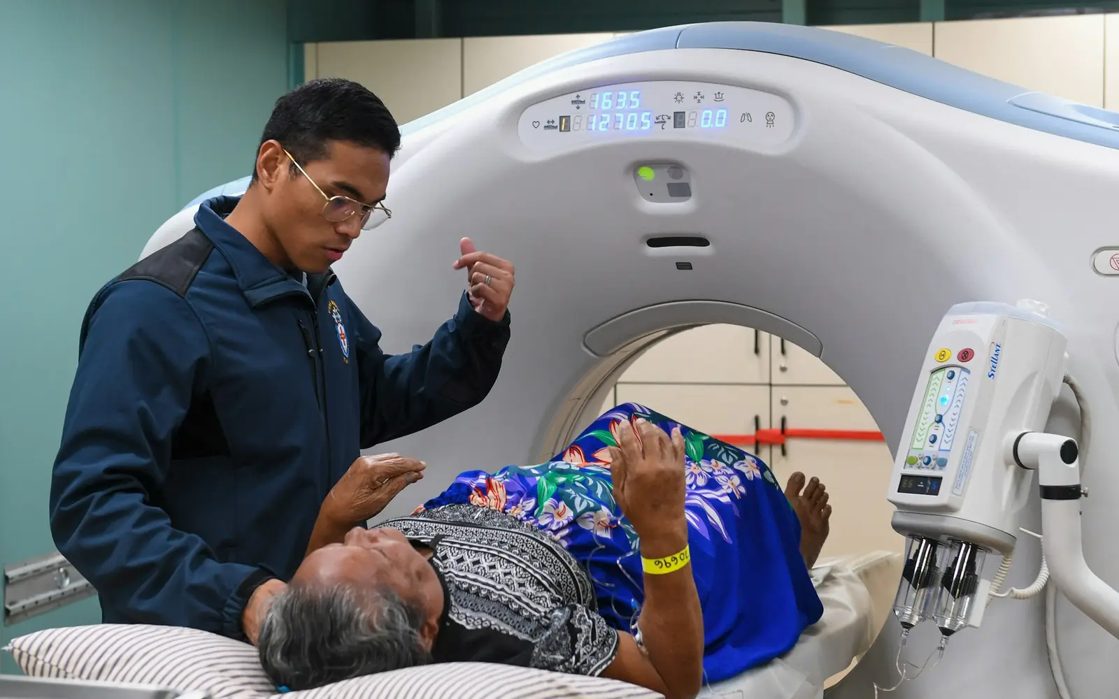 A technologist talks to a patient lying on the table of a CT scanner before a scan.
