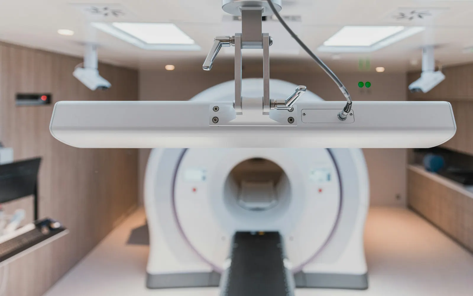 A radiotherapy treatment room with a ring-shaped machine and patient couch, seen past a ceiling-mounted fixture.