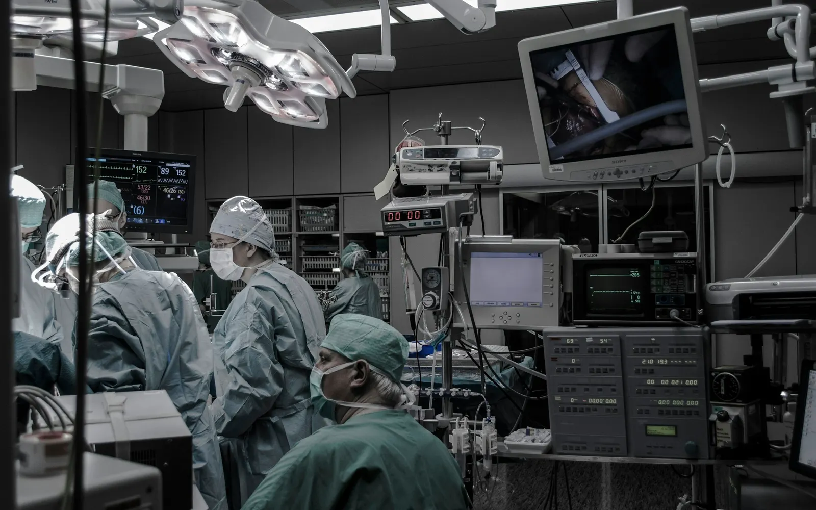 A surgical team works in an operating theatre while a monitor above shows a close-up camera view of the procedure.
